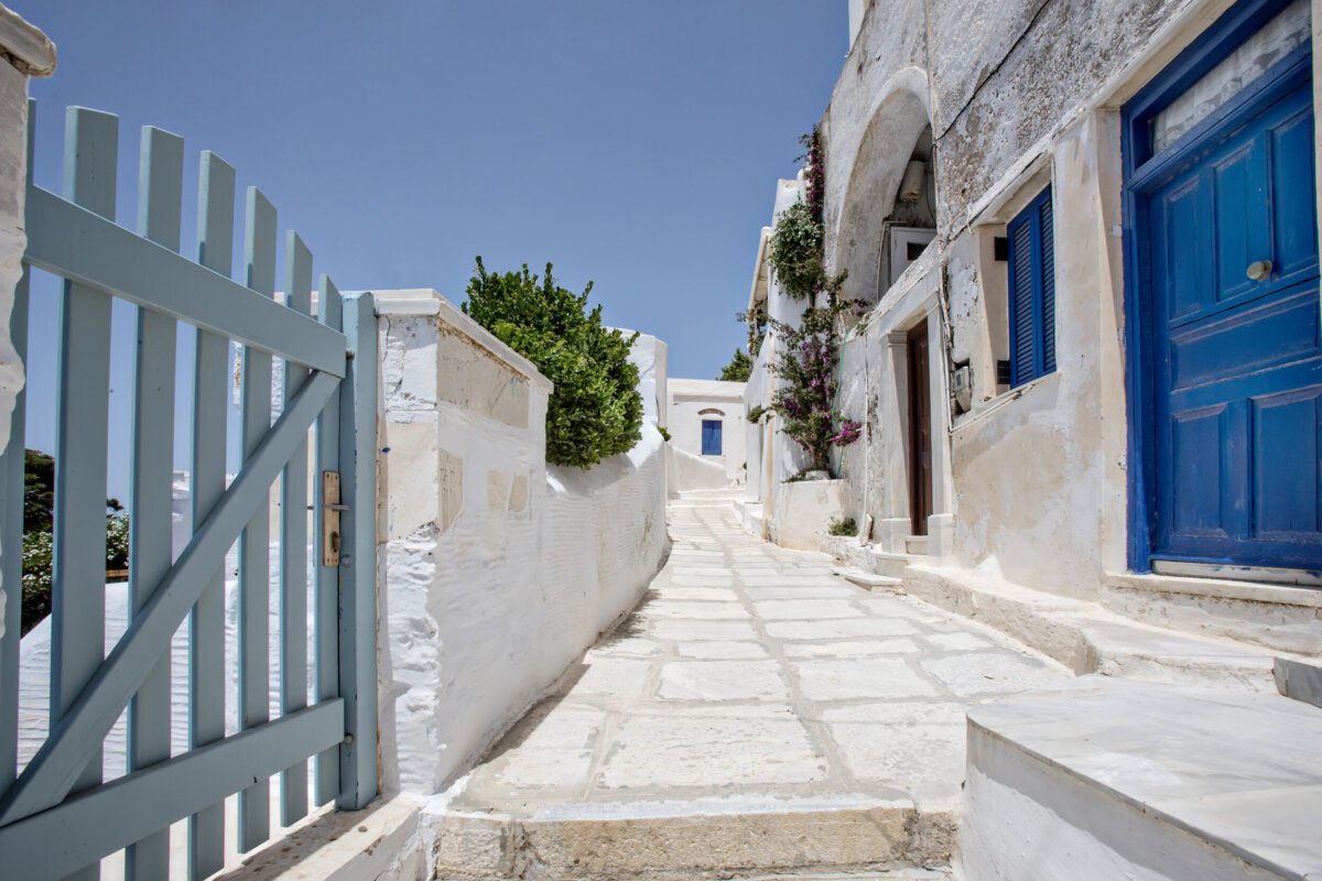 Ασπρισμένο πλακόστρωτο σοκάκι με γαλάζια ξύλινη αυλόπορτα